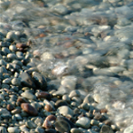 Bild på stenstrand med inrullande våg.